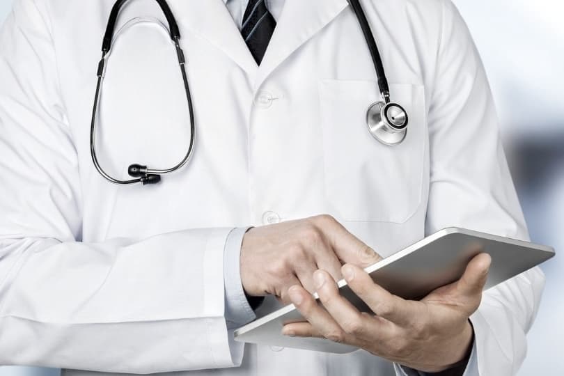 Torso of doctor with white coat on holding ipad