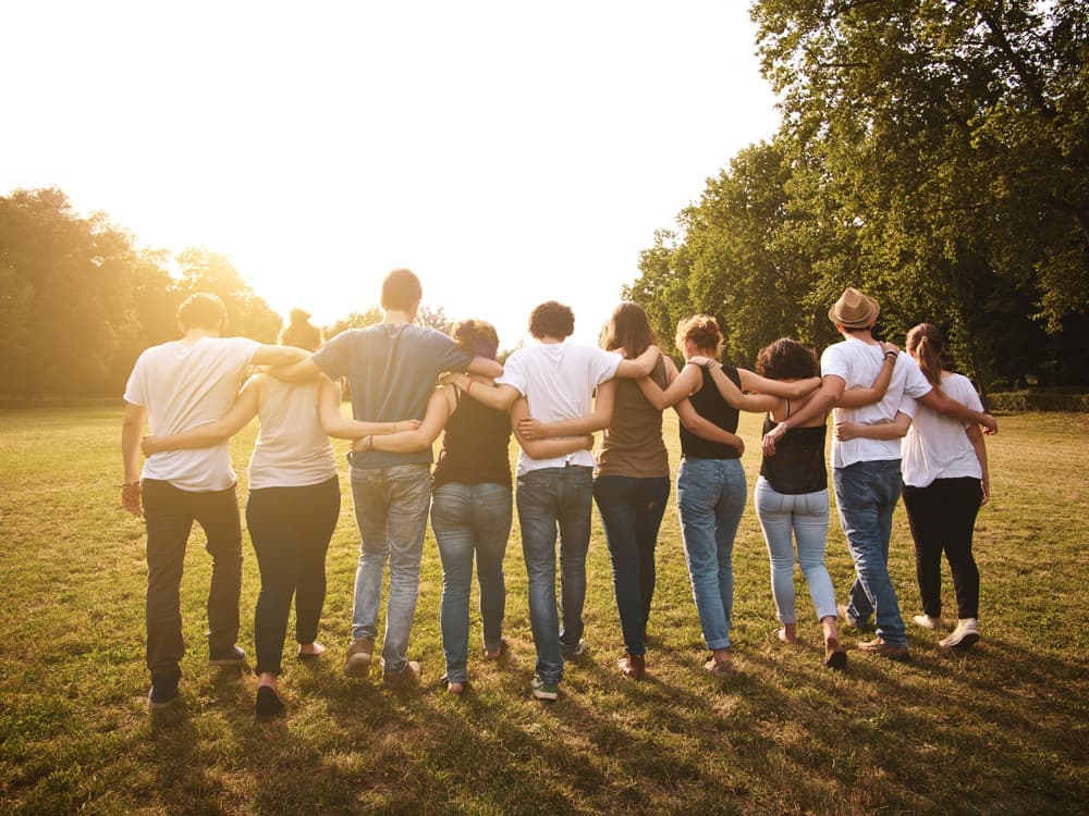 Group of people walking toward the sun with arms linked around each others backs