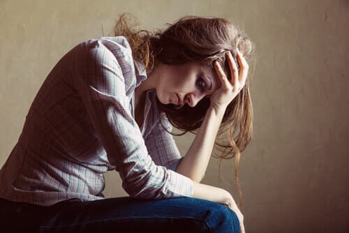 Women sitting with her head down, resting her forehead in her hand. She looks depressed and distraught.