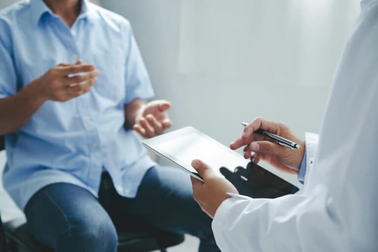 Male in button up shirt sitting on hospital bed talking to doctor