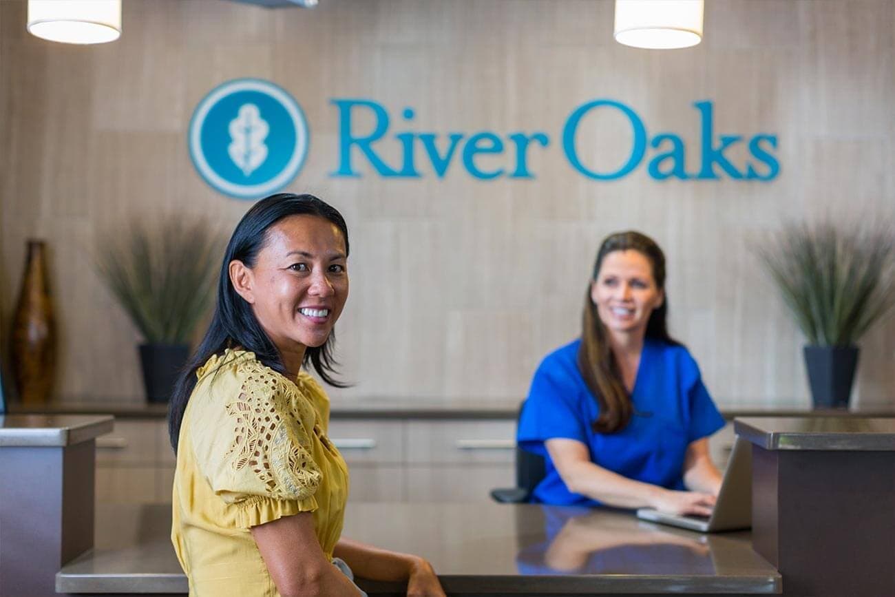 Two female staff members smiling in front of River Oaks reception desk